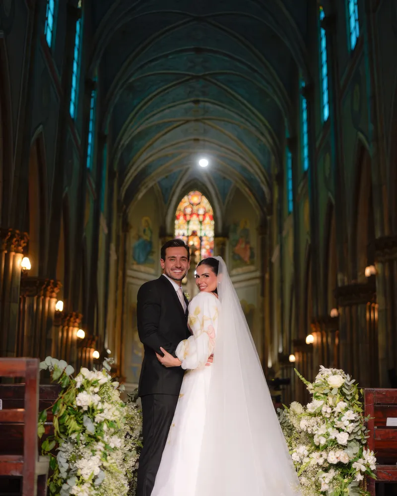 Abraço do casal na nave do Santuário de Santa Teresinha, sob o teto abobadado e o vitral ao fundo
