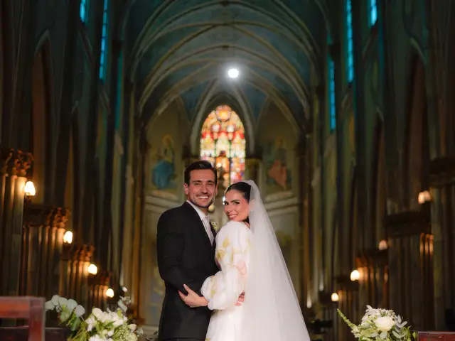 Abraço do casal na nave do Santuário de Santa Teresinha, sob o teto abobadado e o vitral ao fundo