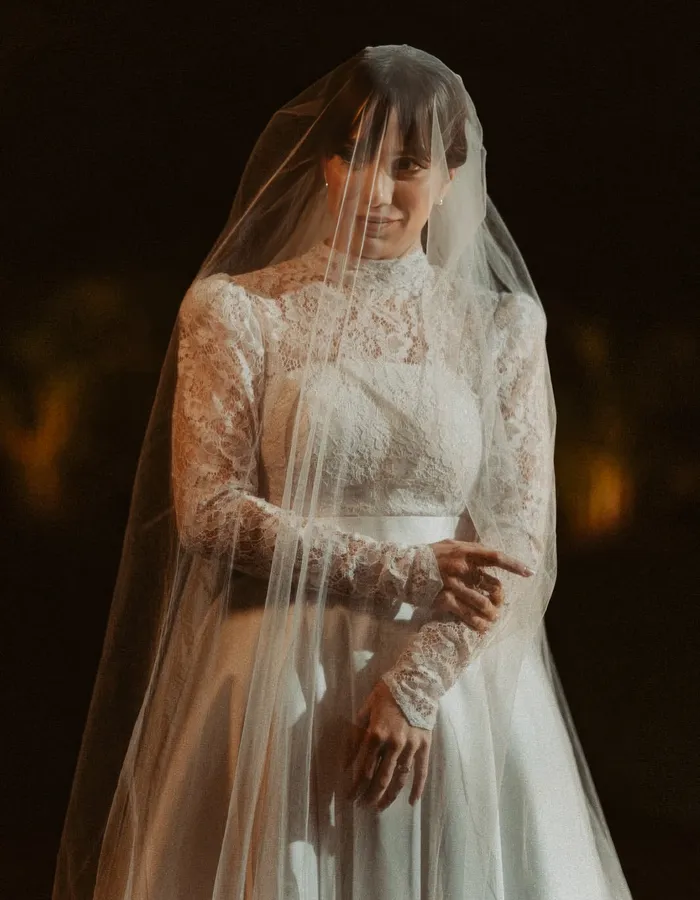 Retrato da noiva com o véu sobre o rosto, em vestido de renda de mangas longas