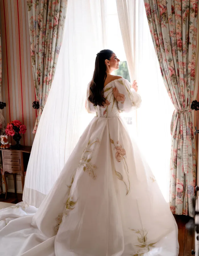 Noiva de costas junto à janela do casarão da Fazenda Fortaleza, detalhe do vestido floral pintado à mão